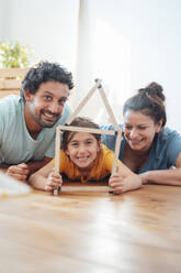 Glückliche Eltern mit Tochter halten Modellhaus auf dem Boden zu Hause - JOSEF21215