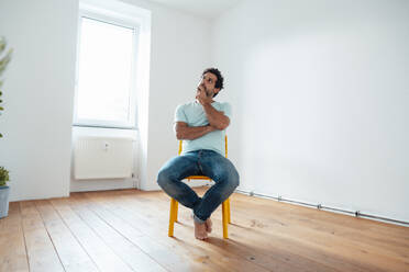 Nachdenklicher Mann sitzt auf einem Stuhl vor einer Wand zu Hause - JOSEF21221