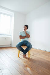 Thoughtful man sitting on chair in front of wall at home - JOSEF21222
