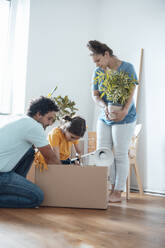 Mother holding plant with father and daughter packing lamp in box - JOSEF21247