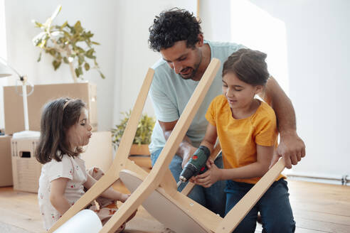 Father and daughter repairing chair with drill machine at home - JOSEF21275