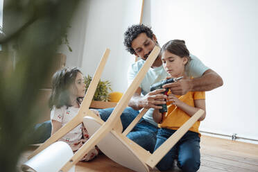 Smiling father and daughter repairing chair with drill machine at home - JOSEF21276