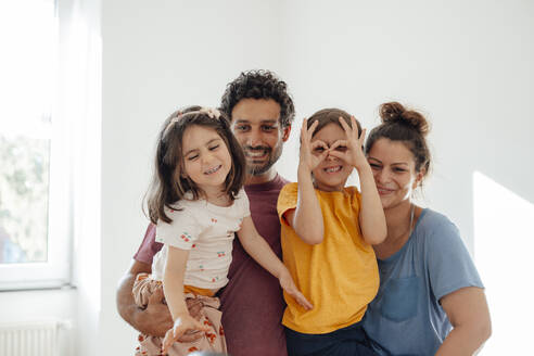 Happy father and mother with daughters in front of wall at home - JOSEF21281