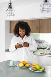 Smiling woman using smart phone in kitchen at home - DLTSF03652