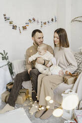 Glückliche Eltern mit ihrer kleinen Tochter, die zu Hause auf dem Sofa sitzt - VBUF00409