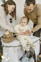 Lächelnde Eltern mit einem kleinen Mädchen, das auf dem Tisch sitzt - VBUF00415