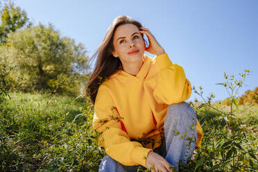 Happy woman sitting in nature on sunny day - MDOF01513