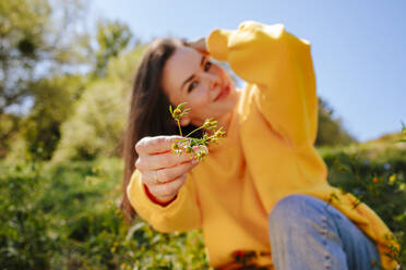 Lächelnde Frau mit Hand im Haar, die eine Blume zeigt - MDOF01516