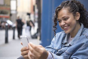 Glückliche junge Frau, die ihr Smartphone auf dem Fußweg benutzt - AMWF01790