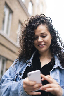 Lächelnde Frau mit lockigem Haar, die ein Smartphone benutzt - AMWF01791