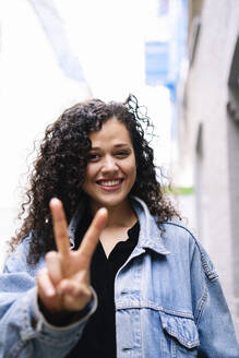 Glückliche junge Frau mit Friedenszeichen-Geste - AMWF01794