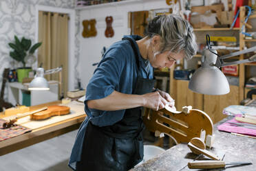 Geigenbauer schnitzt am Schreibtisch in der Werkstatt an einer Geige - MMPF00958