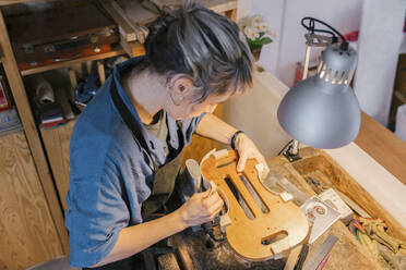 Geigenbauer fertigt Teile einer Geige auf dem Schreibtisch in der Werkstatt - MMPF00967