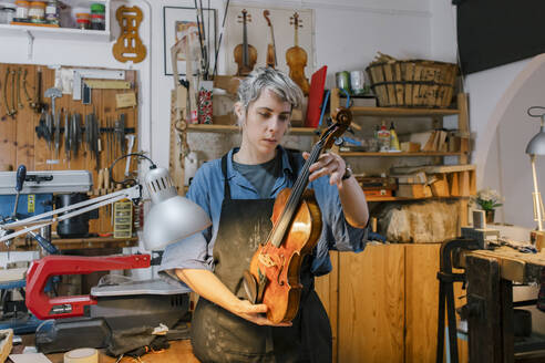 Luthier examining violin in workshop - MMPF00970