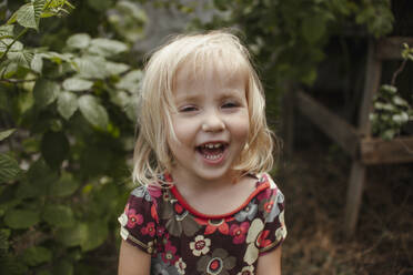 Lächelndes Mädchen in der Nähe von Pflanzen im Garten - ASHF00008