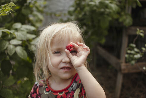 Playful girl holding raspberry in garden - ASHF00009