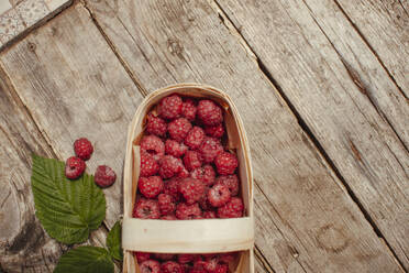 Holzkiste mit Himbeeren neben Blatt auf Tisch - ASHF00013