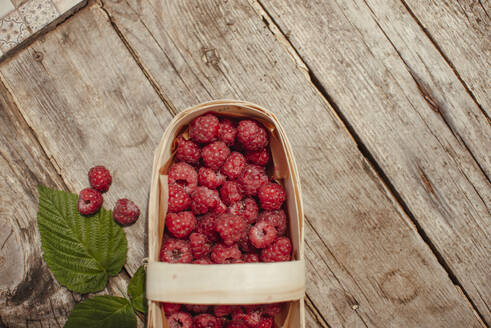 Holzkiste mit Himbeeren neben Blatt auf Tisch - ASHF00013