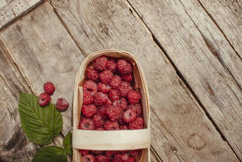 Wooden box with raspberries near leaf on table - ASHF00013