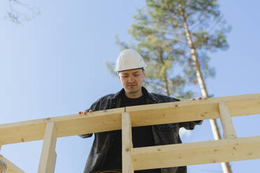 Engineer wearing hardhat examining wood at construction site - SEAF02016