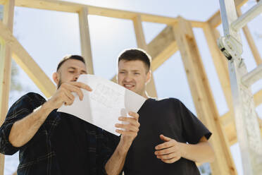 Engineers looking at blueprint and discussing near wooden frame - SEAF02043