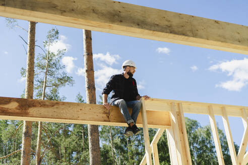 Engineer sitting on wooden frame at construction site - SEAF02048
