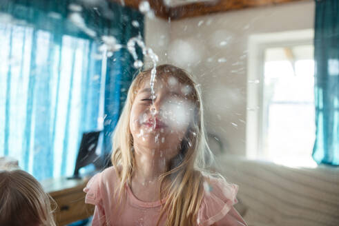 Blondes Mädchen lachend und Wasser aus dem Mund spuckend zu Hause - ASHF00022