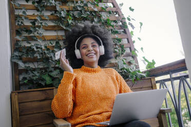 Smiling woman holding credit card and sitting with laptop in balcony - MDOF01555