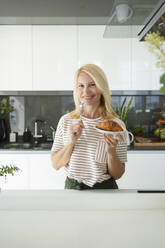 Glückliche Frau hält Croissant in der Küche zu Hause - SVKF01646