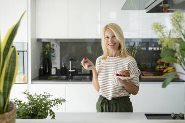 Glückliche Frau hält Teller mit Croissant und Beeren in der Küche zu Hause - SVKF01647