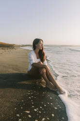 Contemplative woman sitting on sand at beach - SIF00975