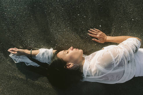 Woman with eyes closed lying on black sand - SIF00989