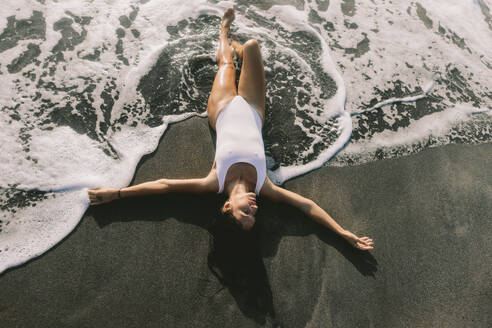 Unbekümmerte Frau auf schwarzem Sand am Strand liegend - SIF01005