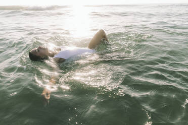 Frau mit geschlossenen Augen schwimmt im Meer am Strand - SIF01008