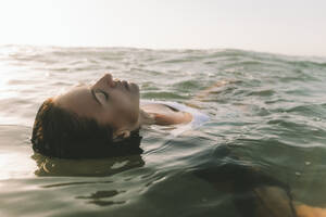 Frau mit geschlossenen Augen beim Schwimmen im Wasser am Strand - SIF01010