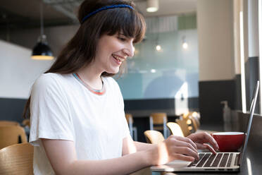 Glücklicher Freiberufler arbeitet am Laptop in einem Café - AMWF01812