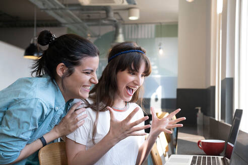 Exycited women looking at laptop in cafe - AMWF01815