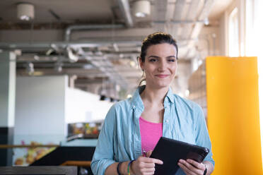 Smiling freelancer holding tablet PC standing in office cafeteria - AMWF01827