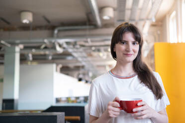 Lächelnde Geschäftsfrau mit Kaffeetasse in einer Büro-Cafeteria - AMWF01828