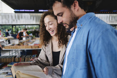 Happy woman with man reading book at bookstore - ASGF04654