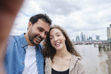 Happy loving couple taking selfie in front of river - ASGF04657