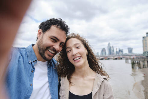 Happy loving couple taking selfie in front of river - ASGF04657