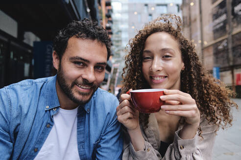 Happy man with woman holding coffee cup at sidewalk cafe - ASGF04661