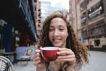 Happy woman holding coffee cup at sidewalk cafe - ASGF04662