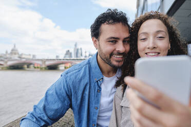 Happy couple taking selfie through smart phone in city - ASGF04668