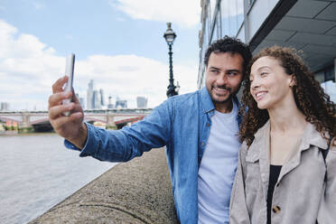 Happy man taking selfie with woman through smart phone - ASGF04669