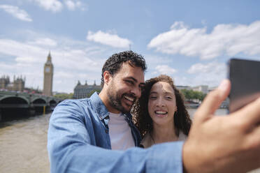 Smiling couple taking selfie under cloudy sky in city - ASGF04673