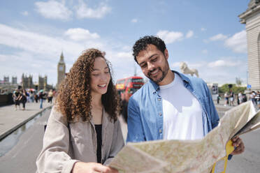 Happy couple reading map on street in city - ASGF04674