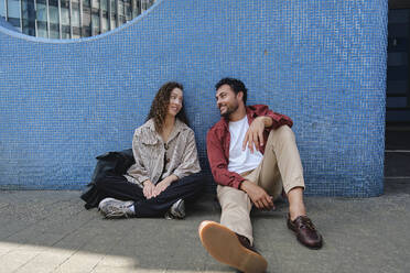 Smiling couple sitting on floor near building - ASGF04678