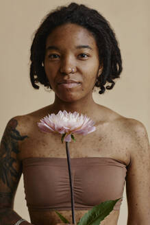 Junge Frau mit Aknenarben hält Blume vor braunem Hintergrund - KPEF00259